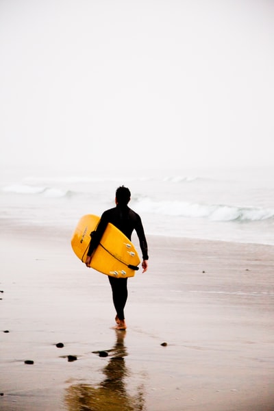 男子拿着黄色的冲浪板,走在海滨白天
